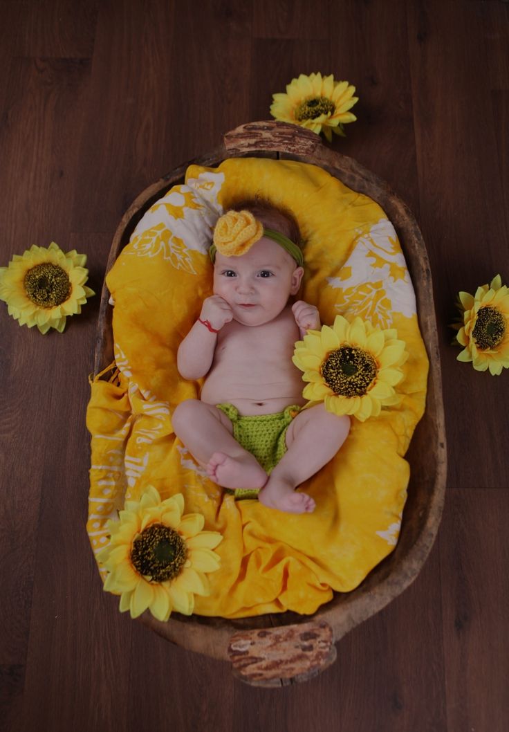 a baby in a basket with sunflowers on the floor