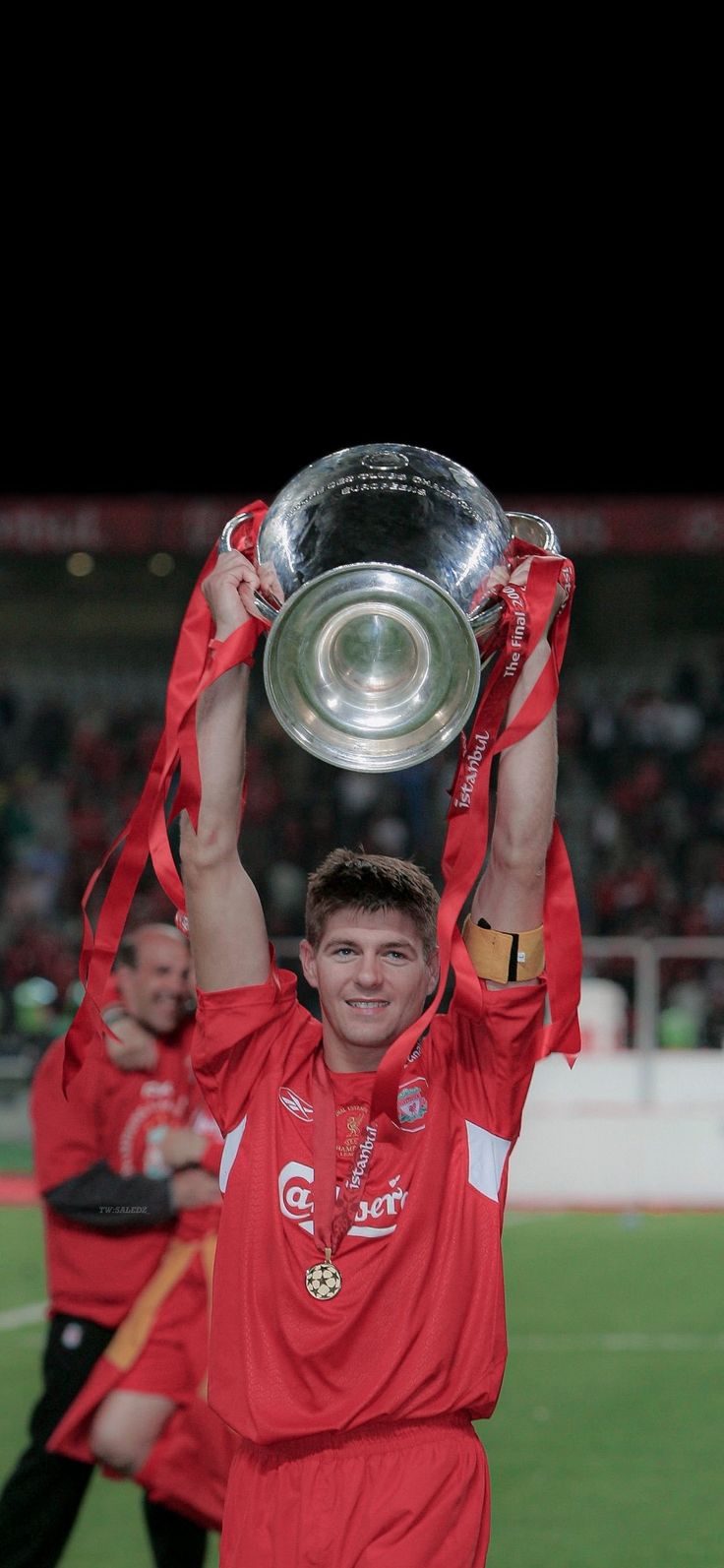 a man holding up a trophy on top of a soccer field with other men in the background