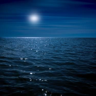 the moon shines brightly over the ocean water as it reflects in the dark blue sky