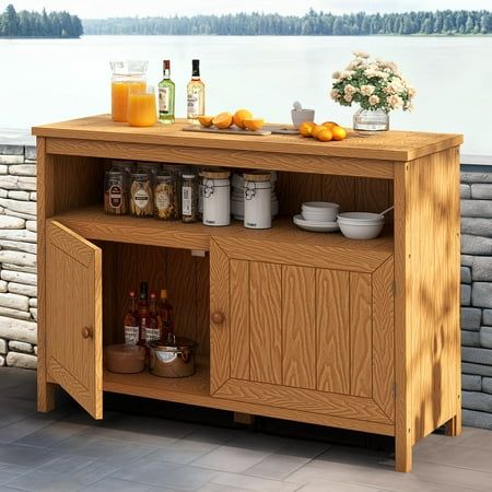 a wooden cabinet with drinks and condiments on the top, next to a stone wall