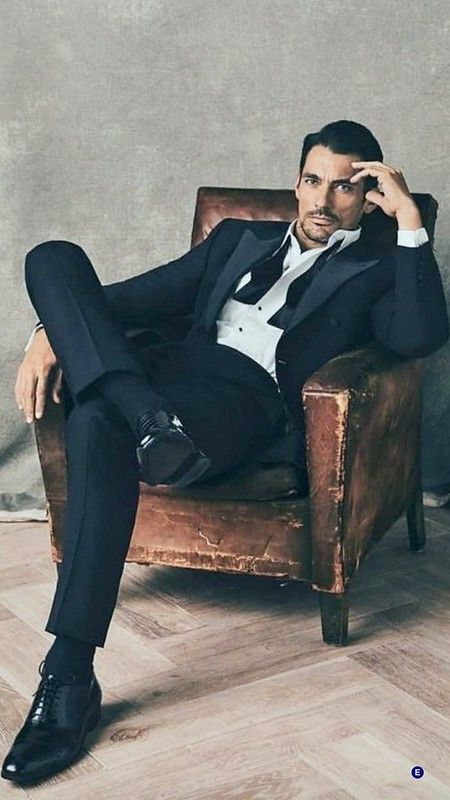 a man in a tuxedo sitting on a chair with his legs crossed and hands behind his head