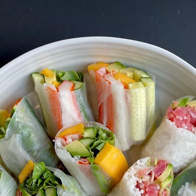 a white bowl filled with different types of sushi rolls on top of a table