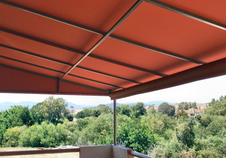 an outdoor covered patio area with tables and chairs under a canopy over looking the trees