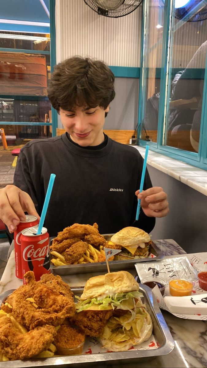 a young man sitting at a table with two trays of food