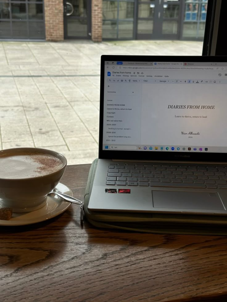 a laptop computer sitting on top of a wooden table next to a cup of coffee