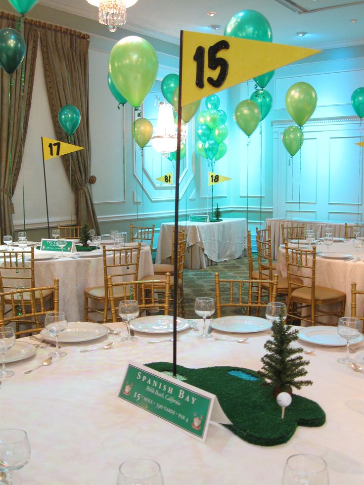 the table is set up for an event with balloons and decorations on it, including a golf green flag