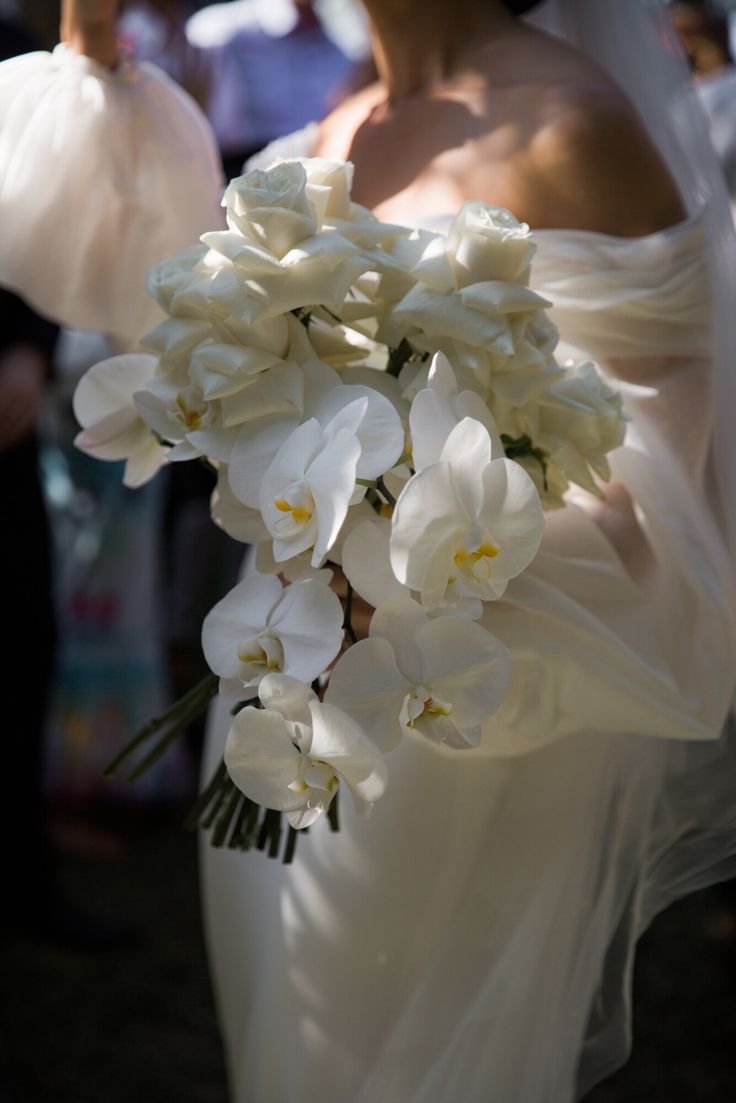 a bride holding a bouquet of white flowers in her hand with other people behind her