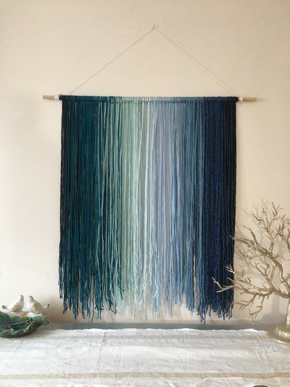 a wall hanging made out of yarn and some branches on top of a white bed