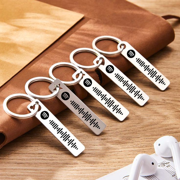 six personalized metal keychains sitting on top of a wooden table next to ear buds