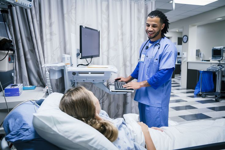 a man in scrubs standing next to a woman on a bed with a laptop