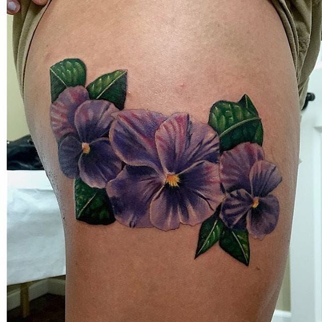 a close up of a woman's thigh with purple flowers on the side and green leaves