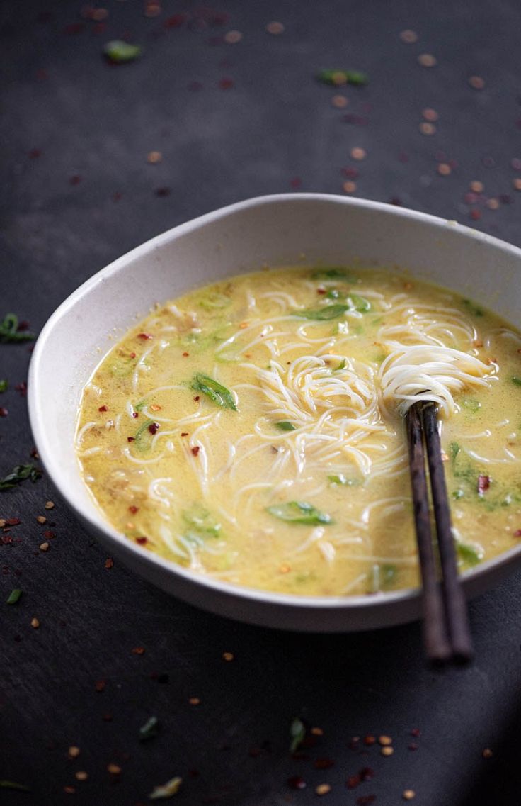 a white bowl filled with soup and noodles on top of a black table next to two chopsticks