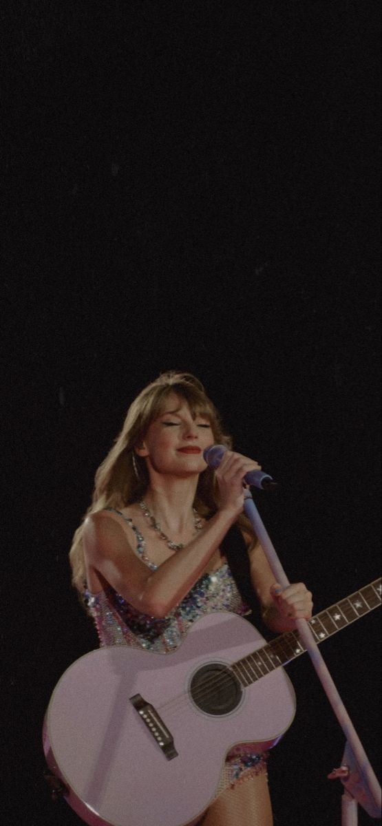 a woman holding a pink guitar and singing into a microphone on stage at a concert