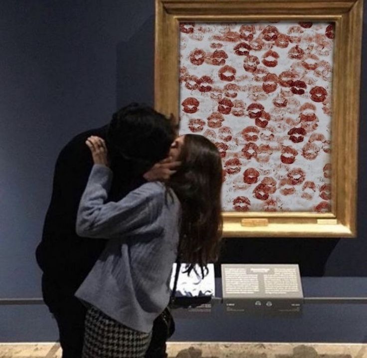 a man and woman are kissing in front of a painting on display at the museum