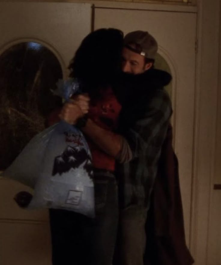 two people hugging each other in front of a door with the light shining on them