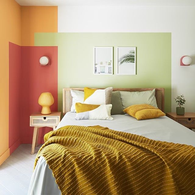 a bed with yellow and orange blankets in a bedroom next to two pictures on the wall