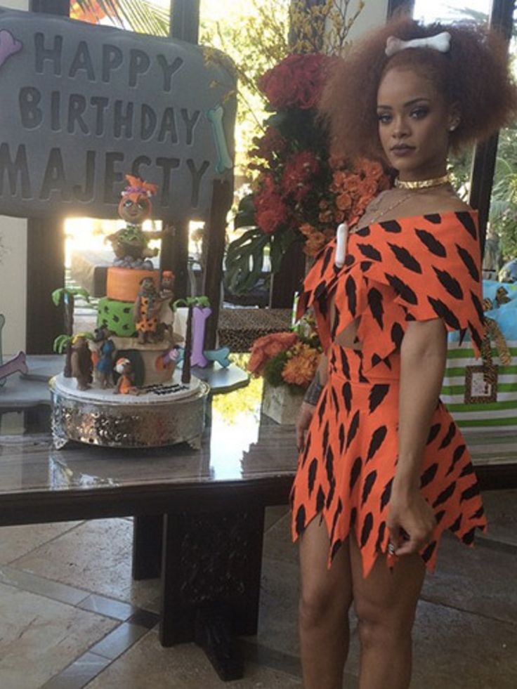 a woman in an orange and black dress standing next to a table with a cake on it