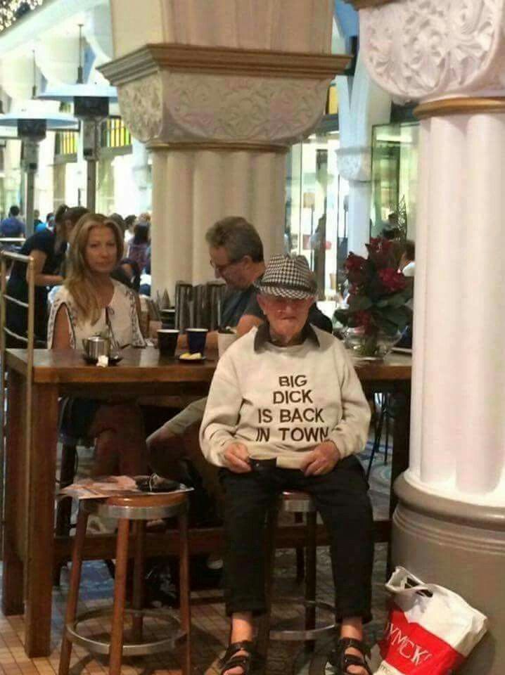 an old man sitting on a stool in front of a table with two other people