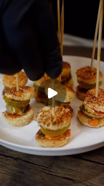 mini sandwiches with toothpicks in them on a white plate, being held by someone