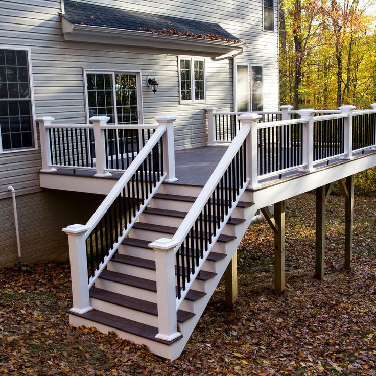 a white deck with stairs and railings in front of a gray house on a fall day