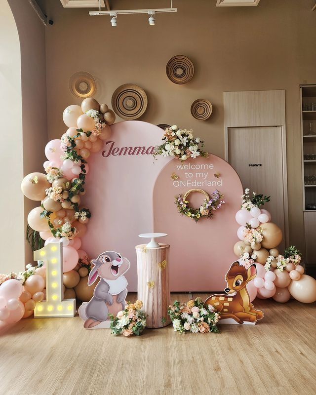 a pink backdrop with balloons and flowers on the floor in front of an arch that says, i do my own one