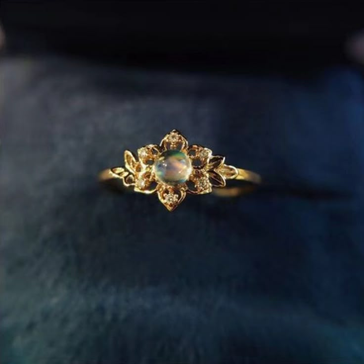 a gold ring with an opal center surrounded by small white flowers on top of a blue velvet surface