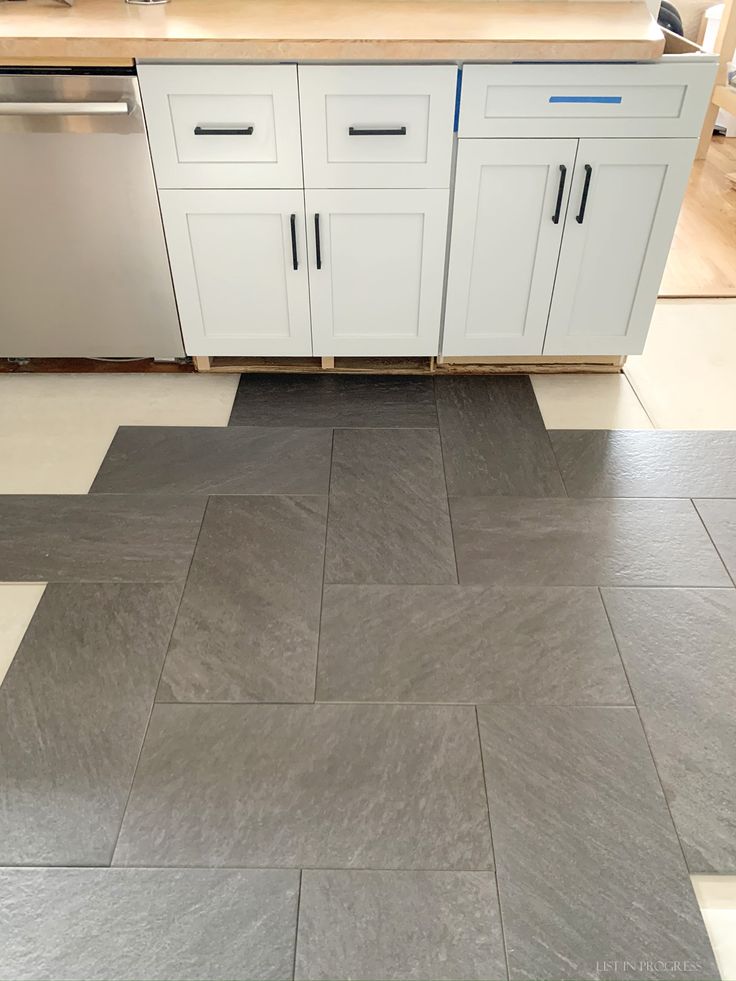 a kitchen with white cabinets and gray floor tiles on the floor, next to a dishwasher