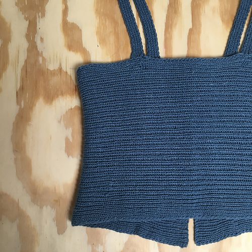 a crocheted blue top is laying on a wooden surface with the bottom part missing