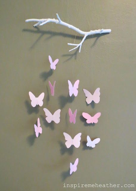 several pink and white butterflies are hanging on a wall next to a twig branch