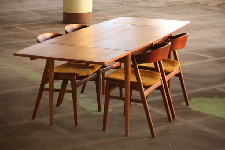 a wooden table and four chairs in an empty room with concrete flooring on the ground