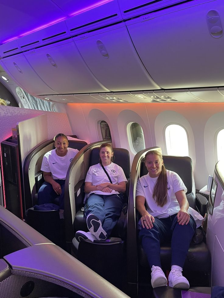 two women sitting on seats in the aisle of an airplane with purple lighting behind them