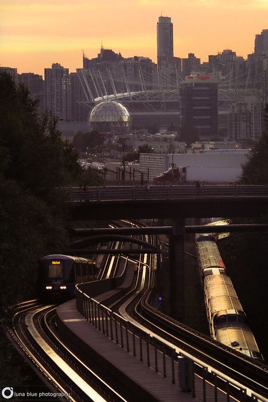 a train is traveling down the tracks in front of a cityscape at sunset