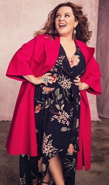 a woman in a black and pink dress with a red cape over her shoulders smiling