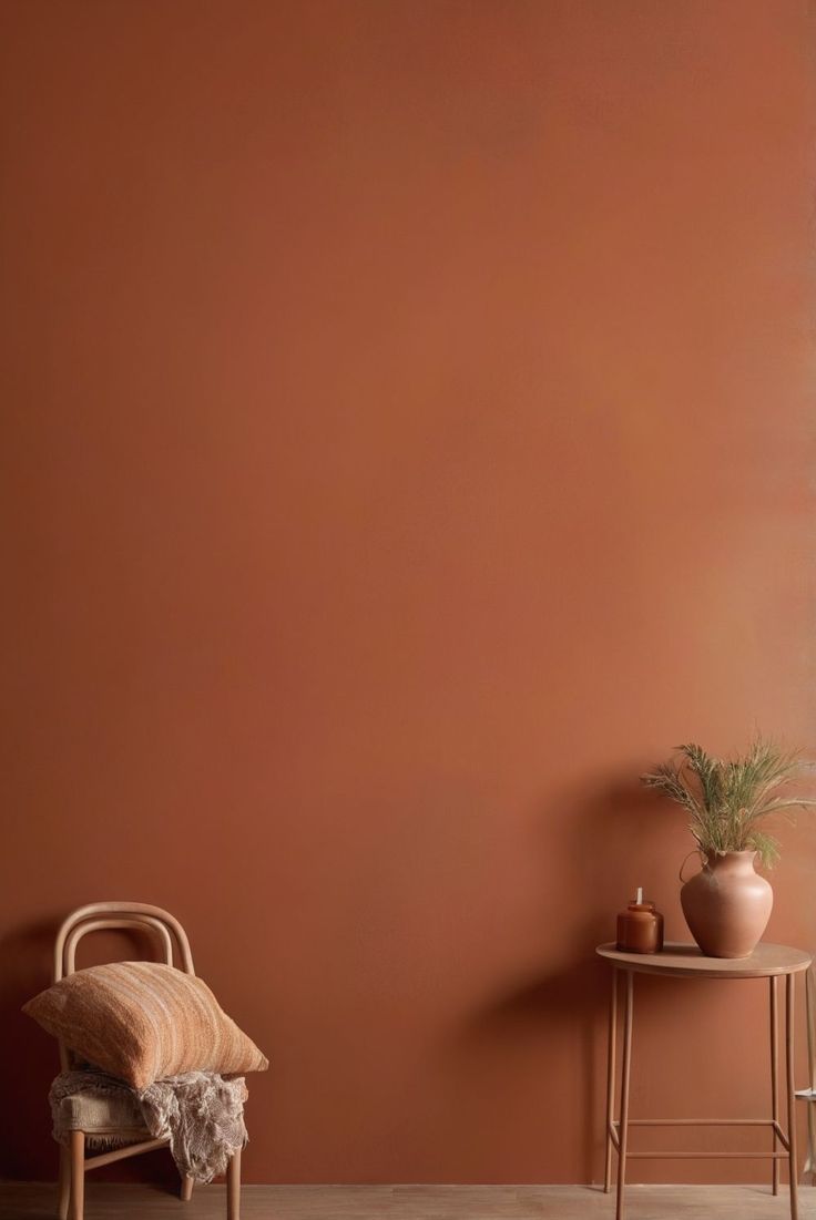 two chairs and a table in front of an orange wall with potted plants on it