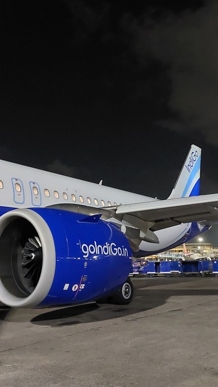 a blue and white jet airliner sitting on top of an airport tarmac at night