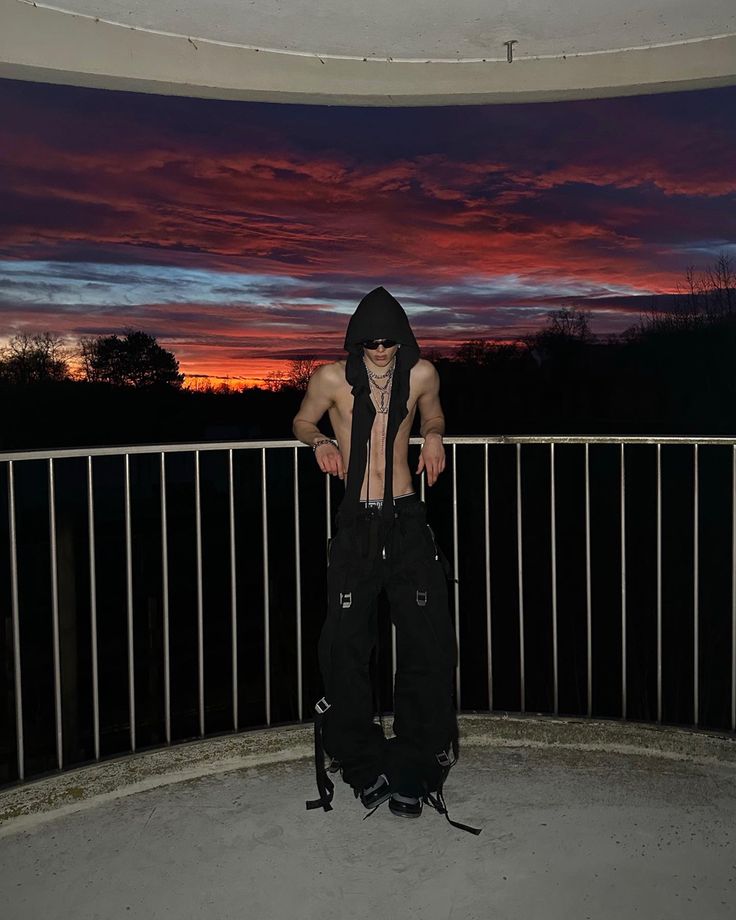 a shirtless man standing on top of a balcony next to a fence at sunset