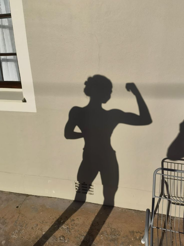 a shadow of a person standing in front of a wall with a shopping cart next to it