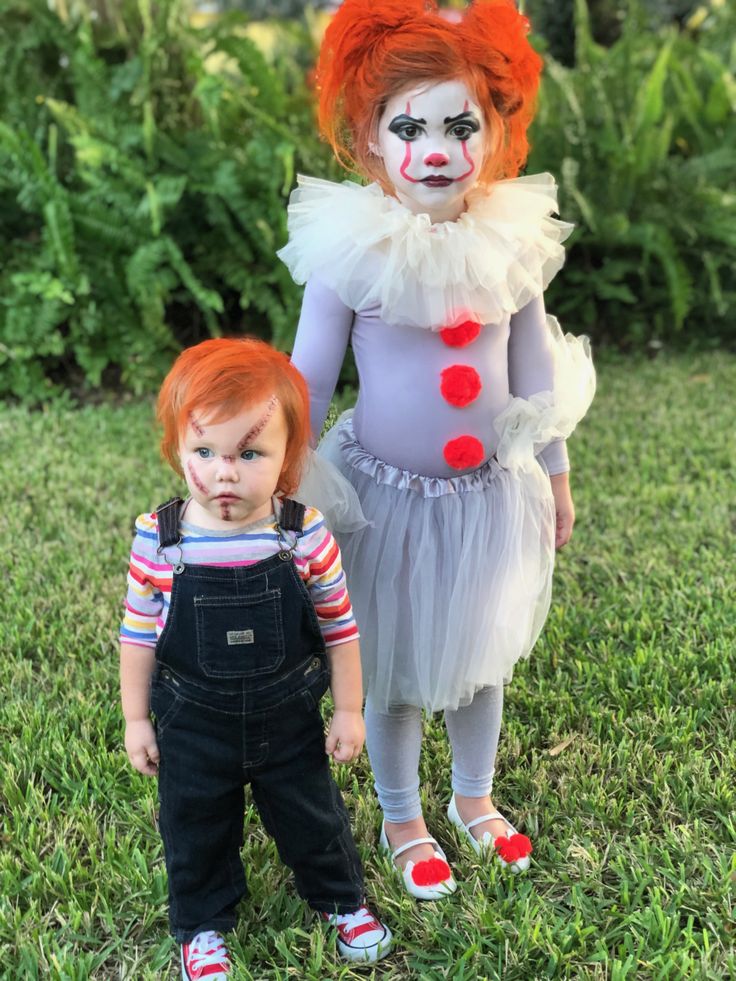 two children dressed up as clowns standing in the grass with their faces painted red and white