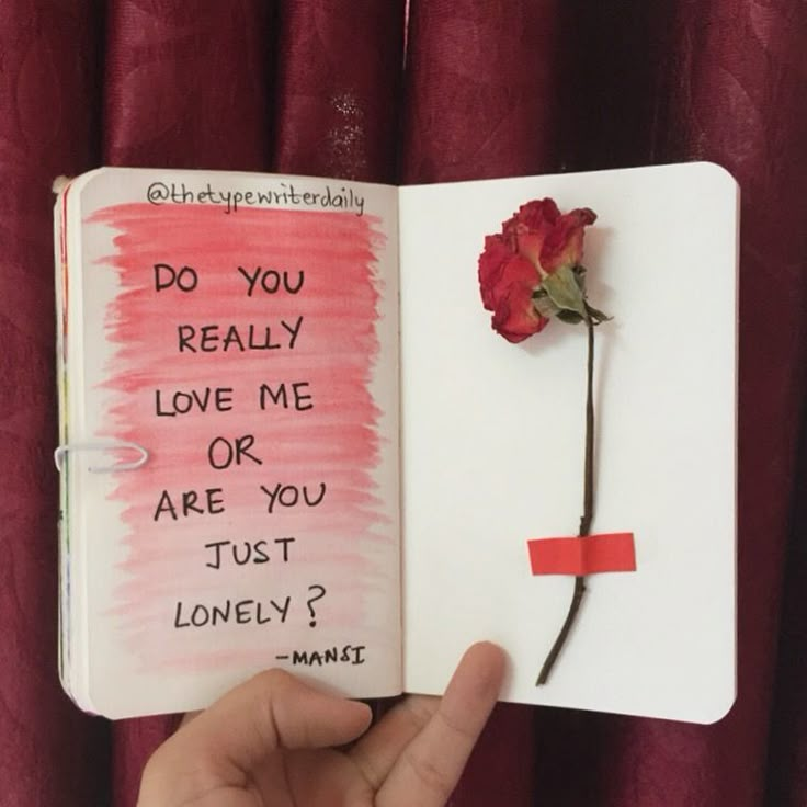 a hand holding an open book with writing on it and a flower sticking out of the pages