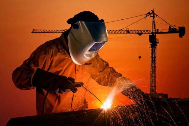 a man welding in front of a building under construction with the sun setting behind him