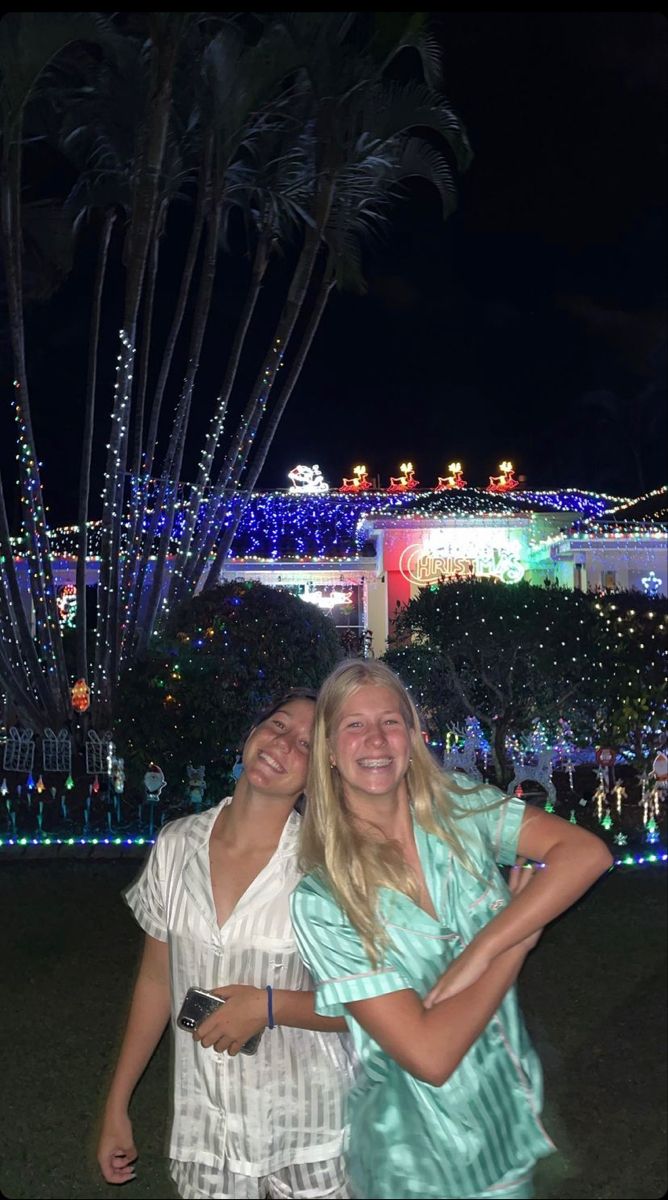 two women standing next to each other in front of a building with lights on it