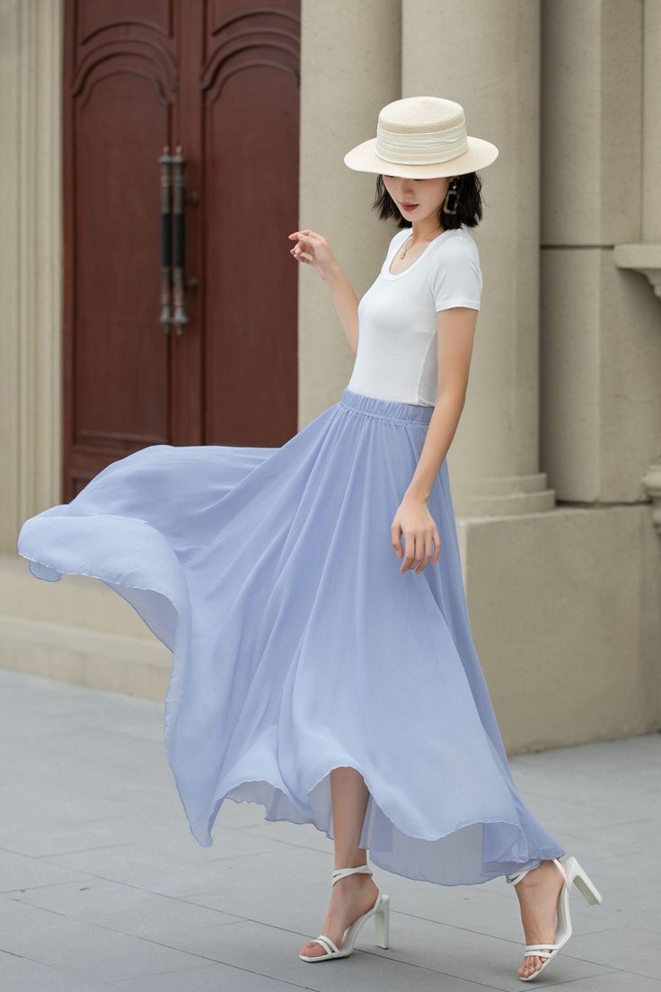 a woman in a white hat and blue dress is walking down the street with her hand on her hip