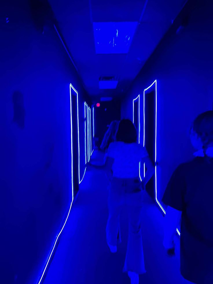 two people walking down a dark hallway with blue light on the walls and flooring