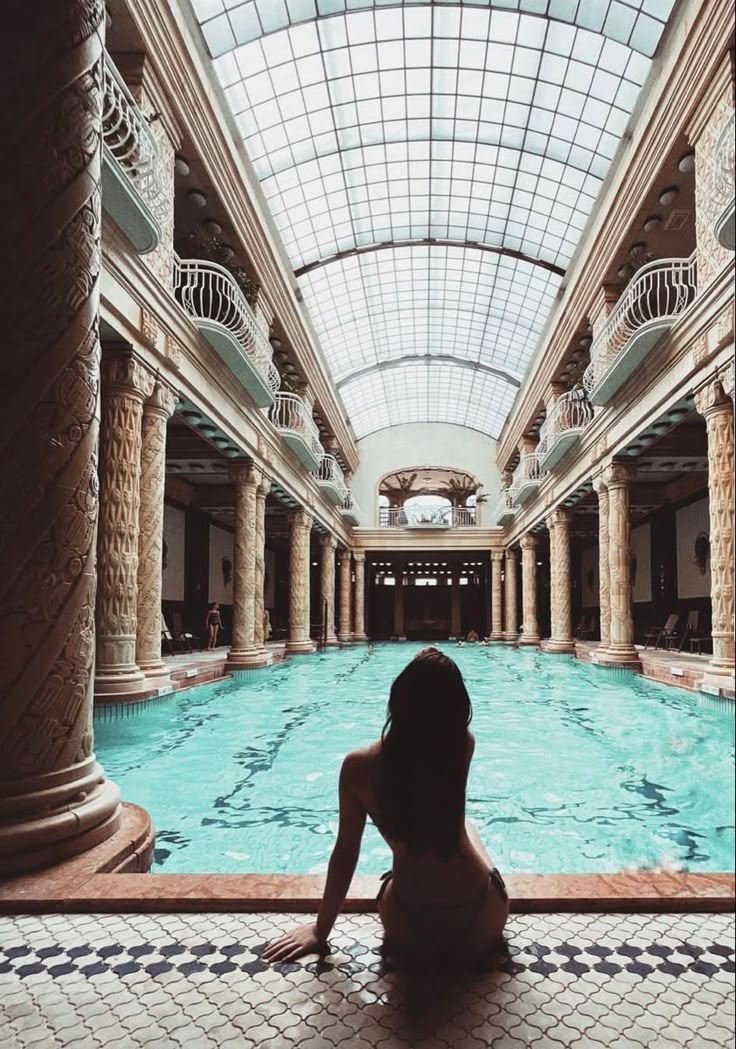 a woman sitting on the floor in front of a swimming pool surrounded by stone pillars