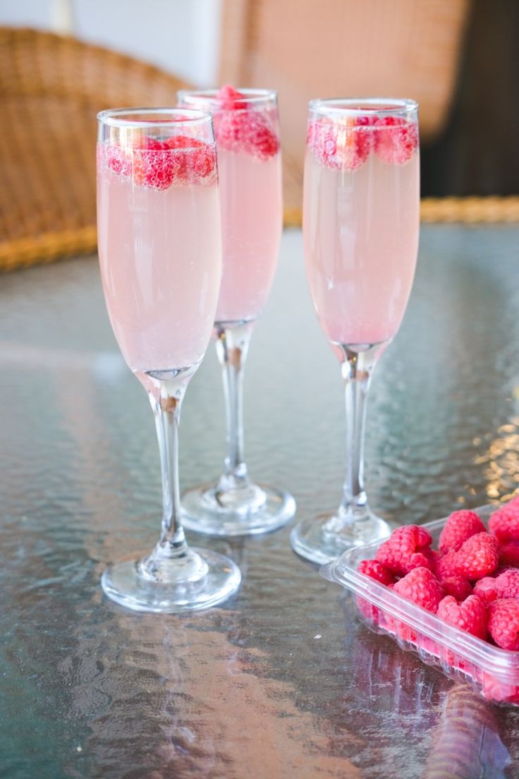 three wine glasses with raspberries in them sitting on a table next to some strawberries