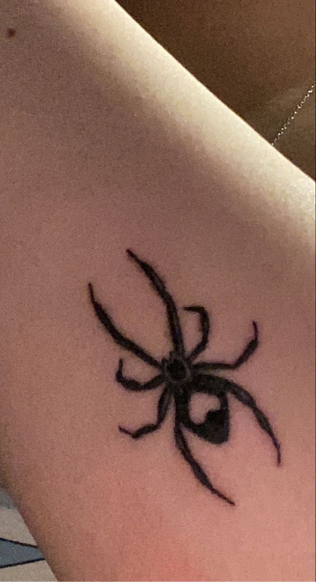 a black spider tattoo on the back of a woman's shoulder