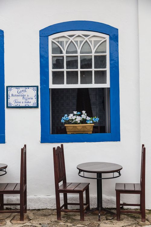 three chairs and a table in front of a white building with blue trim around the windows