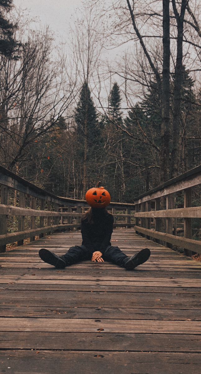 a person sitting on a bridge with an orange pumpkin in their head