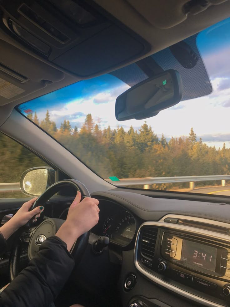 a person driving a car on a highway with trees in the background and clouds in the sky