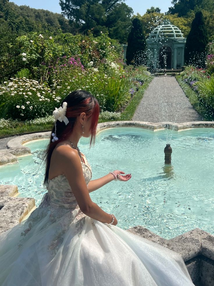 a woman in a wedding dress looking at a fountain